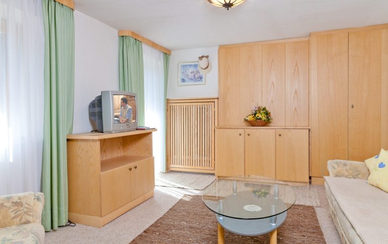 Gemütliches Wohnzimmer mit hellen Holzmöbeln, Pflanzen und einem Fernseher.