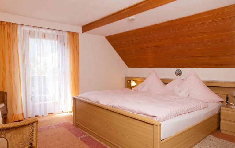 Helles Schlafzimmer mit Doppelbett und Fenster, Möblierung in warmen Tönen.