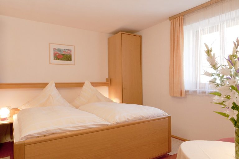 Helles, gemütliches Schlafzimmer mit Doppelbett, Schrank und Fenster. 